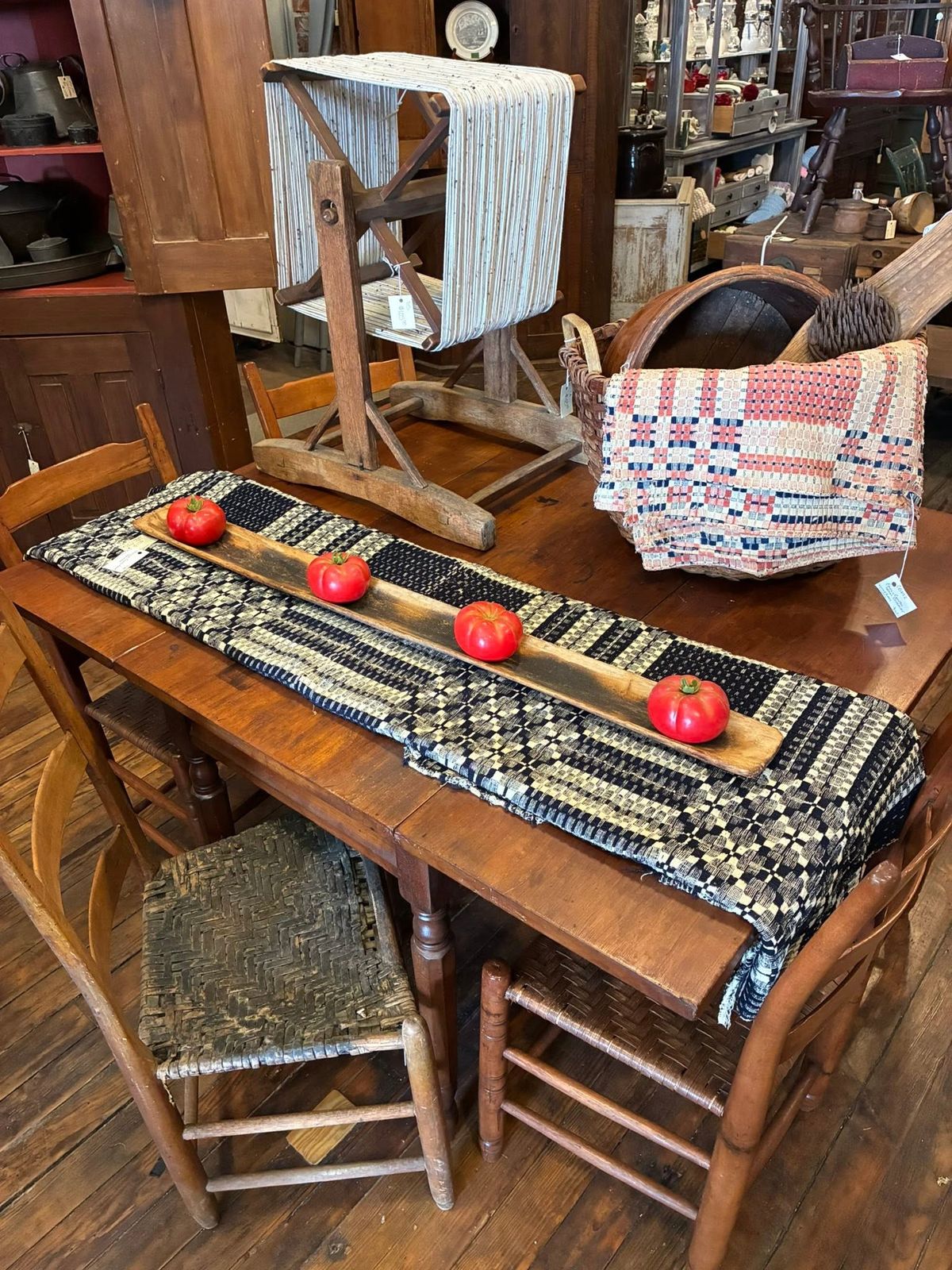 A primitive farm table set with a woven runner, tomatoes and a splint basket at Tinner's Anvil