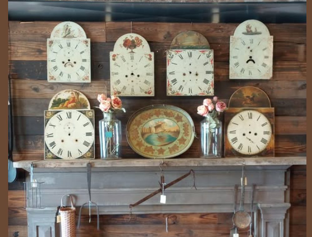 A row of early painted clock faces displayed on a wood-paneled mantel
