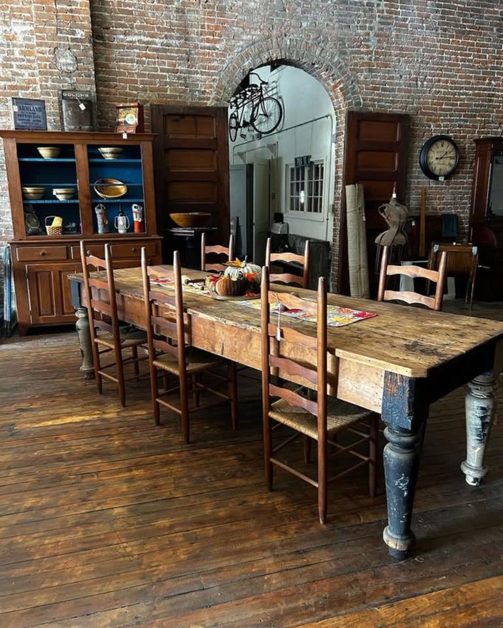 Interior of Tinner's Anvil: a long primitive farm table and ladder-back chairs against exposed brick walls